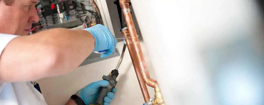 Water heater repair technician testing copper pipe connections and controls in San Jose, CA